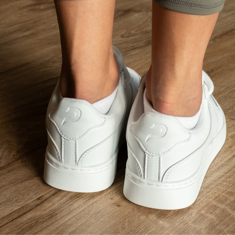 Back view of white low-top Pulse Dance Shoes dance sneakers on a wooden floor, with white ankle socks and heel logos